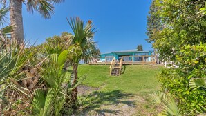 A modern building with a blue facade, a grassy lawn, and a wooden deck. - DIRECT OCEANFRONT BEACH HOME! PRIVATE BEACH ACCESS! (New Smyrna Beach)