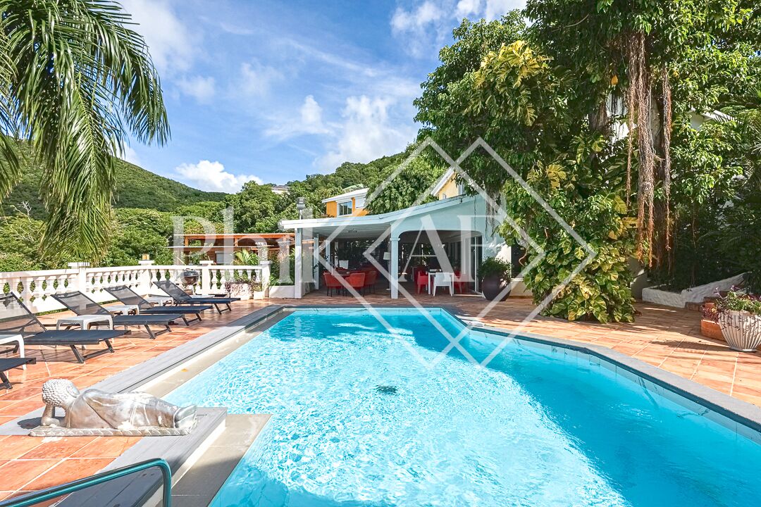 A swimming pool with lounge chairs, a covered seating area, and a mountainous backdrop.