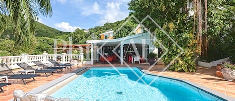 A swimming pool with lounge chairs, a covered seating area, and a mountainous backdrop.