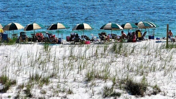 Una playa con filas de sillas y sombrillas, arena al frente y el océano al fondo.
