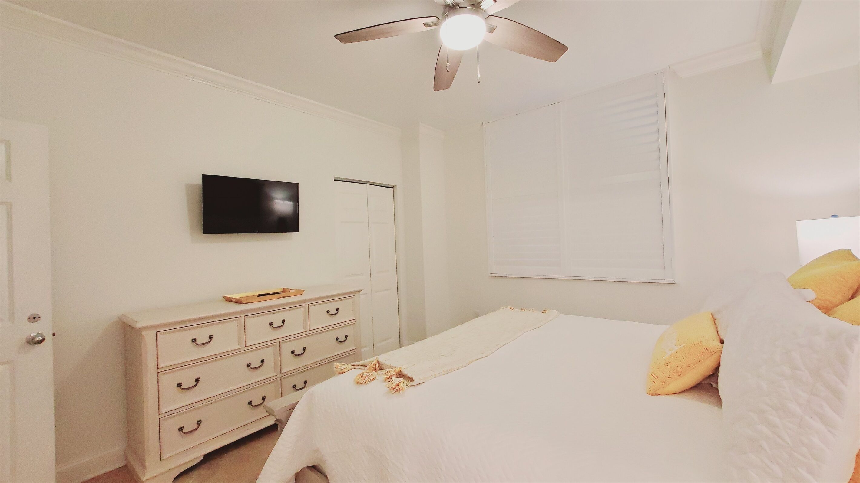 A bedroom with a bed, a dresser, a television, and a ceiling fan.