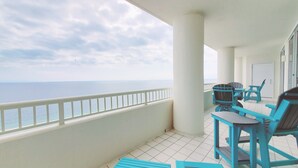 Un balcón con vista al mar, que incluye una baranda blanca, sillas azules y una mesa.