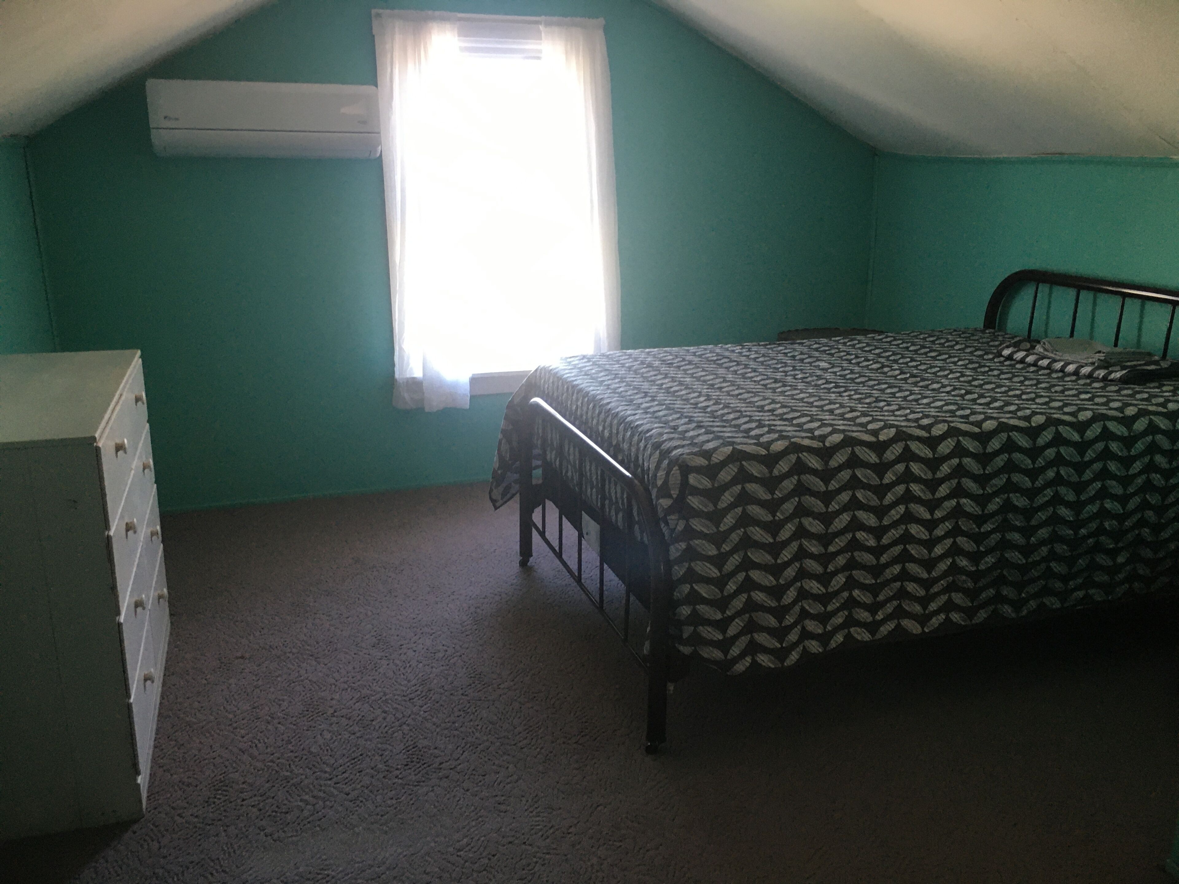 A room with a bed, a dresser, and a window with curtains.