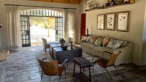 A cozy living room with a stone floor, a sofa, two chairs, a coffee table, and a bookshelf. - Alma Liebre Viñedos del Valle (Valle de Guadalupe)