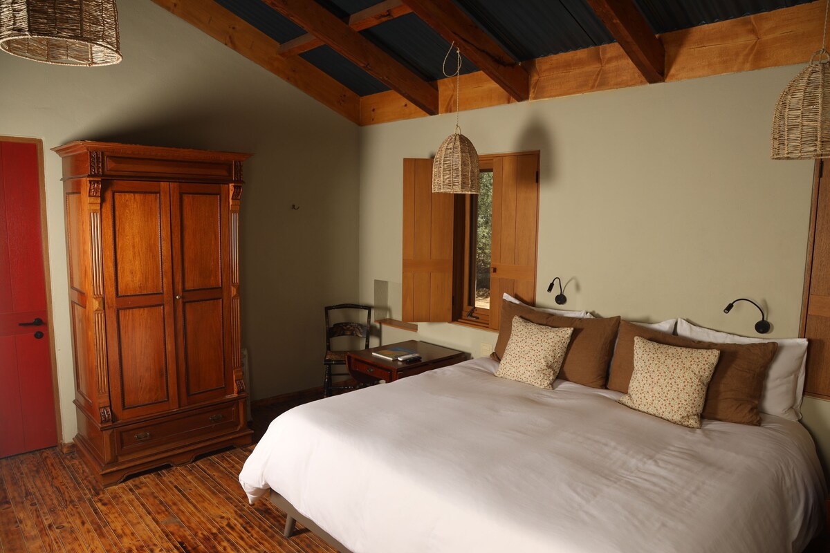 A bedroom with a large bed, wooden wardrobe, and a small table.