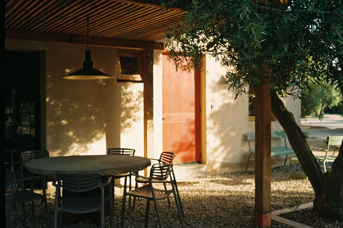 An outdoor seating area with a round table and chairs, a hanging light fixture, and a tree providing shade.
