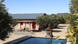 A pool area with a building in the background, surrounded by trees and a clear sky. - Alma Liebre Viñedos del Valle (Valle de Guadalupe)