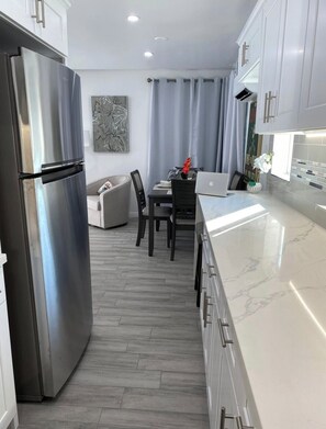 A modern kitchen with a stainless steel refrigerator, a dining area with a table and chairs, and a white marble countertop.