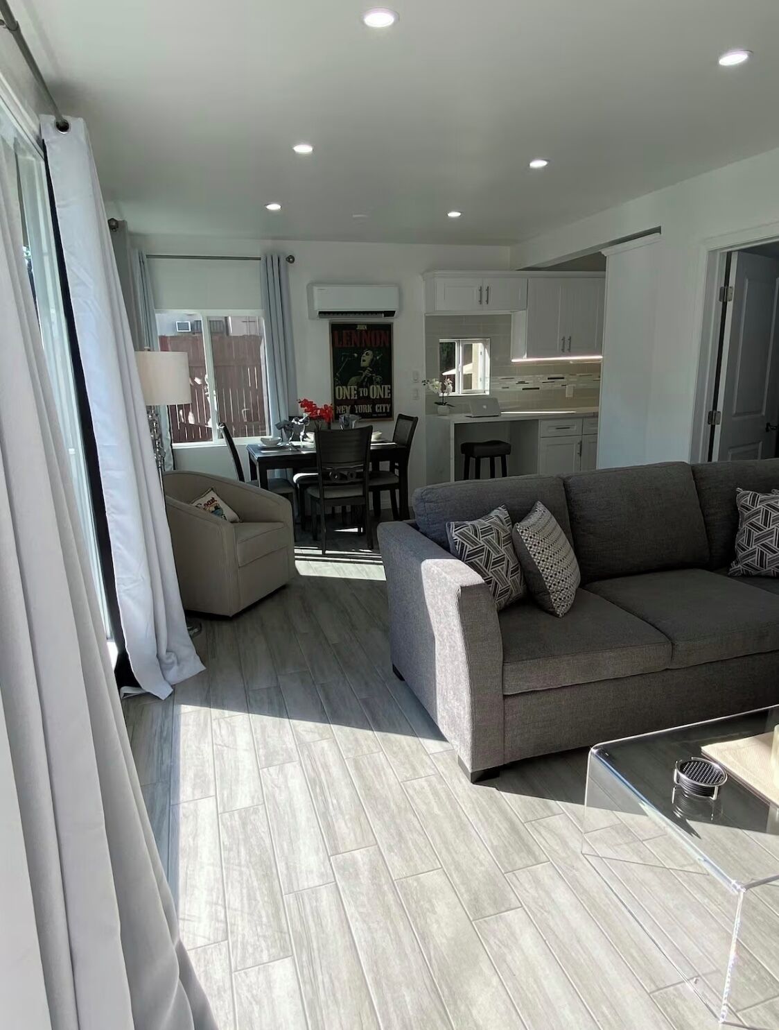 A modern living room with a grey sofa, a dining table, and a kitchen in the background.