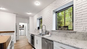 A modern kitchen with white brick walls, stainless steel appliances, and a view of greenery outside. - Lakefront Luxury Cabin Retreat with Jacuzzi & Party Dock (Gainesville)