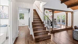 A modern interior with a wooden staircase, a dining area with outdoor seating, and a large window providing natural light. - Lakefront Luxury Cabin Retreat with Jacuzzi & Party Dock (Gainesville)