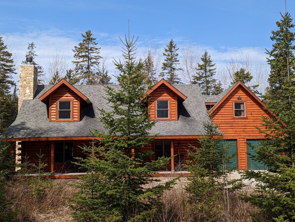 A log cabin with a stone chimney, multiple windows, and a green door.