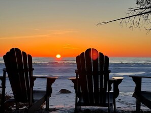 Två Adirondack-stolar placerade så att de vetter mot en solnedgång över havet.