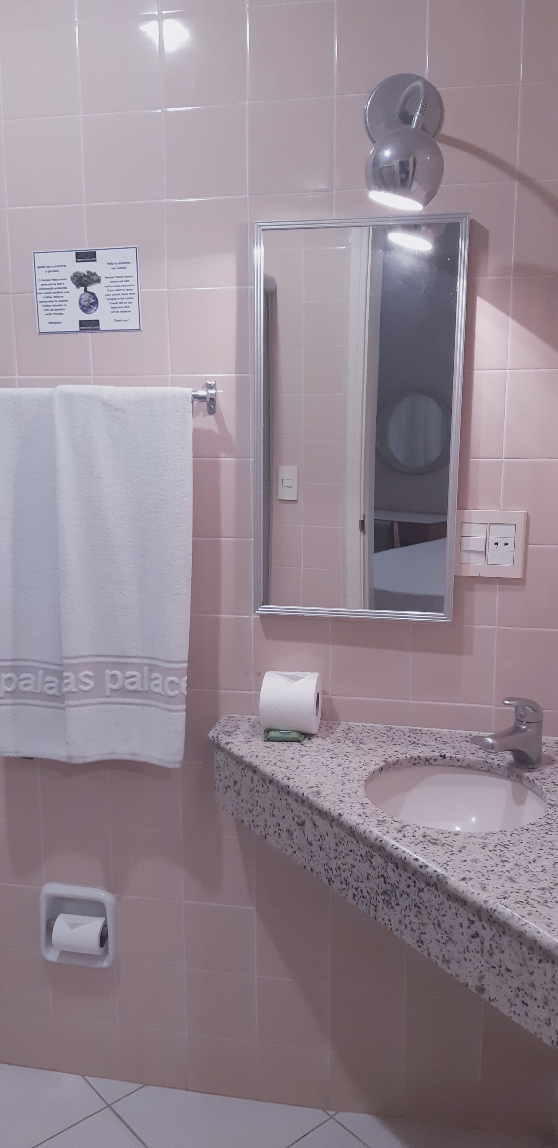 A bathroom with pink tiles, a white towel, a sink with a mirror, and a toilet paper holder.