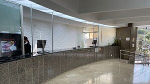 Un espace d’accueil moderne avec un comptoir en marbre aux lignes courbes, un téléviseur à écran plat affichant un menu et une cloison en verre.