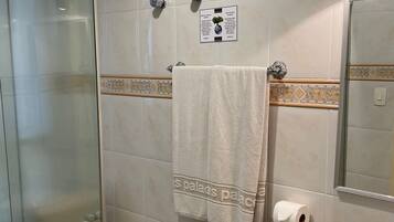 Un baño con cabina de ducha de vidrio, inodoro, lavamanos con encimera de mármol, toalla en un perchero y espejo instalado en la pared.