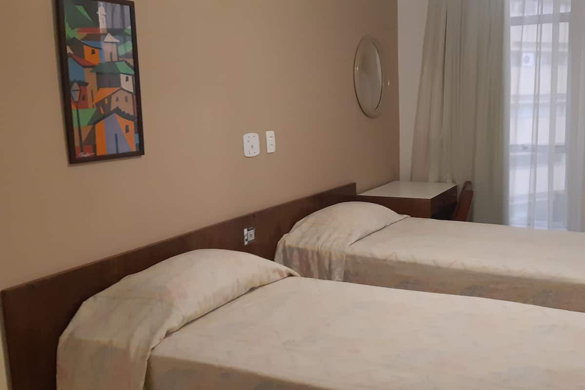 Une chambre d’hôtel avec deux lits simples, une petite table, un miroir fixé au mur et un tableau.