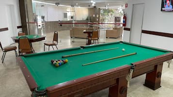 A pool table with balls, chairs, and a billiard cue.