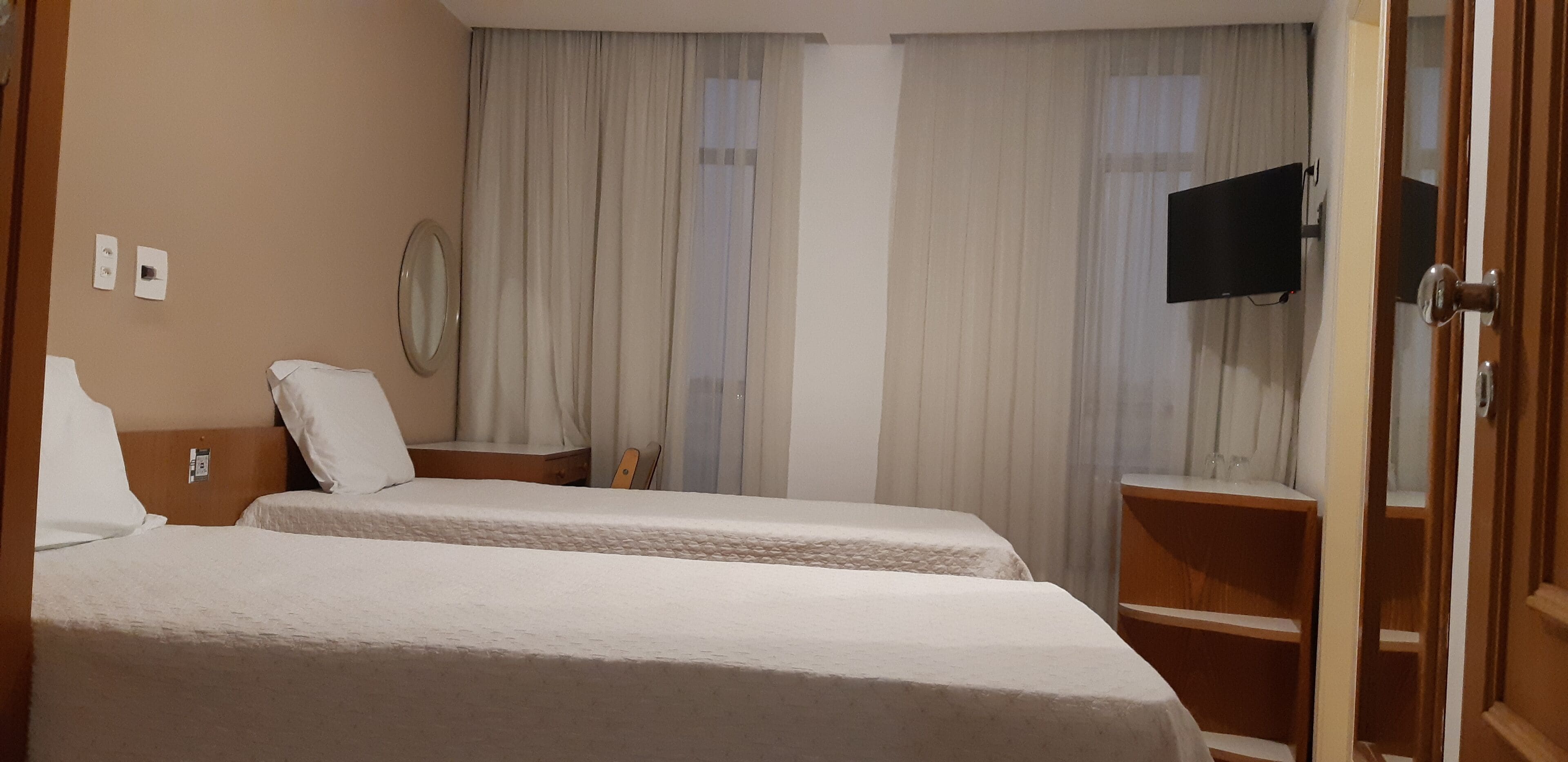A hotel room with two beds, a TV mounted on the wall, and a wooden wardrobe.