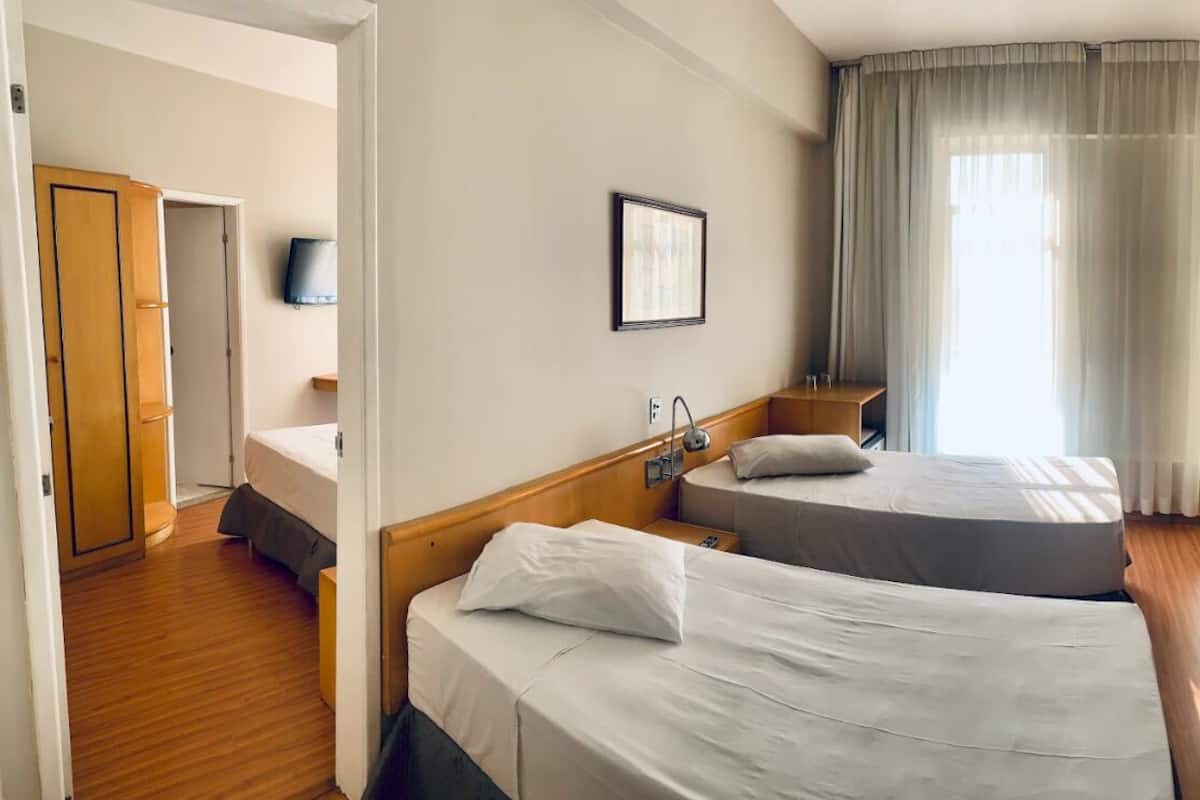 Une chambre d’hôtel avec deux lits, une télévision, une table de chevet, une fenêtre avec des rideaux et une armoire en bois.