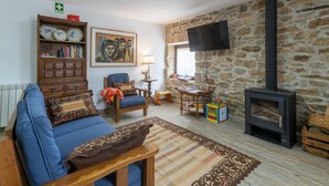Ein gemütliches Wohnzimmer mit einer Couch, einem Sessel, einem Holztisch und einer Steinwand. Außerdem ist ein Kamin und ein Fernseher zu sehen.