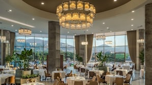 A spacious dining area with round tables, elegant chandeliers, and large windows offering a city view. - DoubleTree by Hilton Manisa (Manisa)