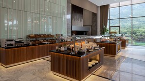 A modern breakfast bar with a wooden finish, a large window offering a view of the outdoors, and a variety of food and beverage options. - DoubleTree by Hilton Manisa (Manisa)