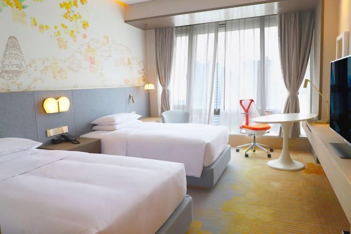 A hotel room with two beds, a desk, a chair, a TV, and a window with curtains.