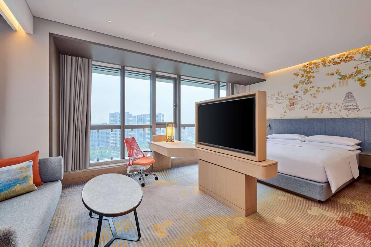 Ein Hotelzimmer mit einem großen Bett, einem Fernseher, einem Schreibtisch, einem Sessel und einer Couch.