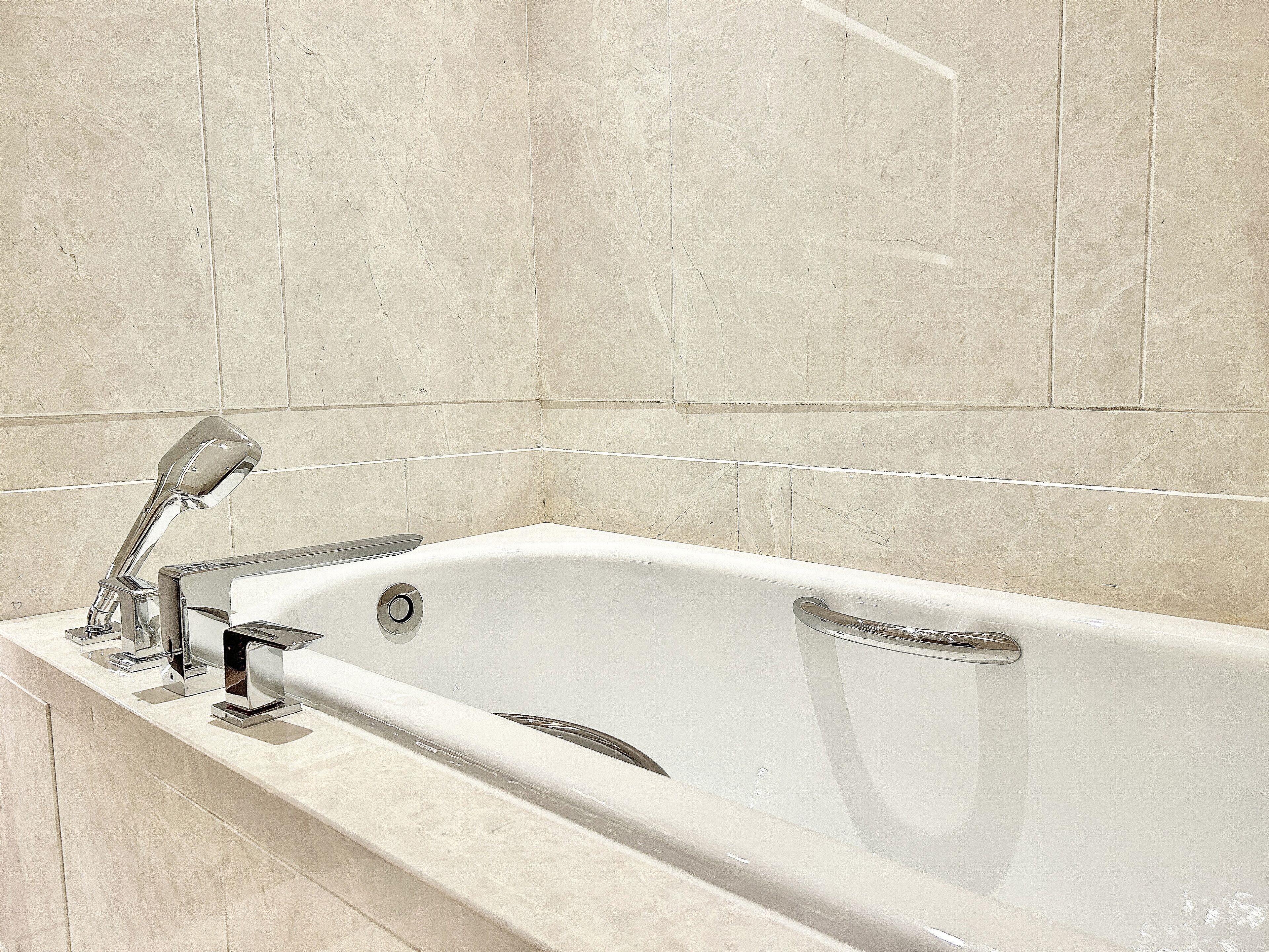 A modern bathroom with a freestanding bathtub, chrome fixtures, and marble walls.