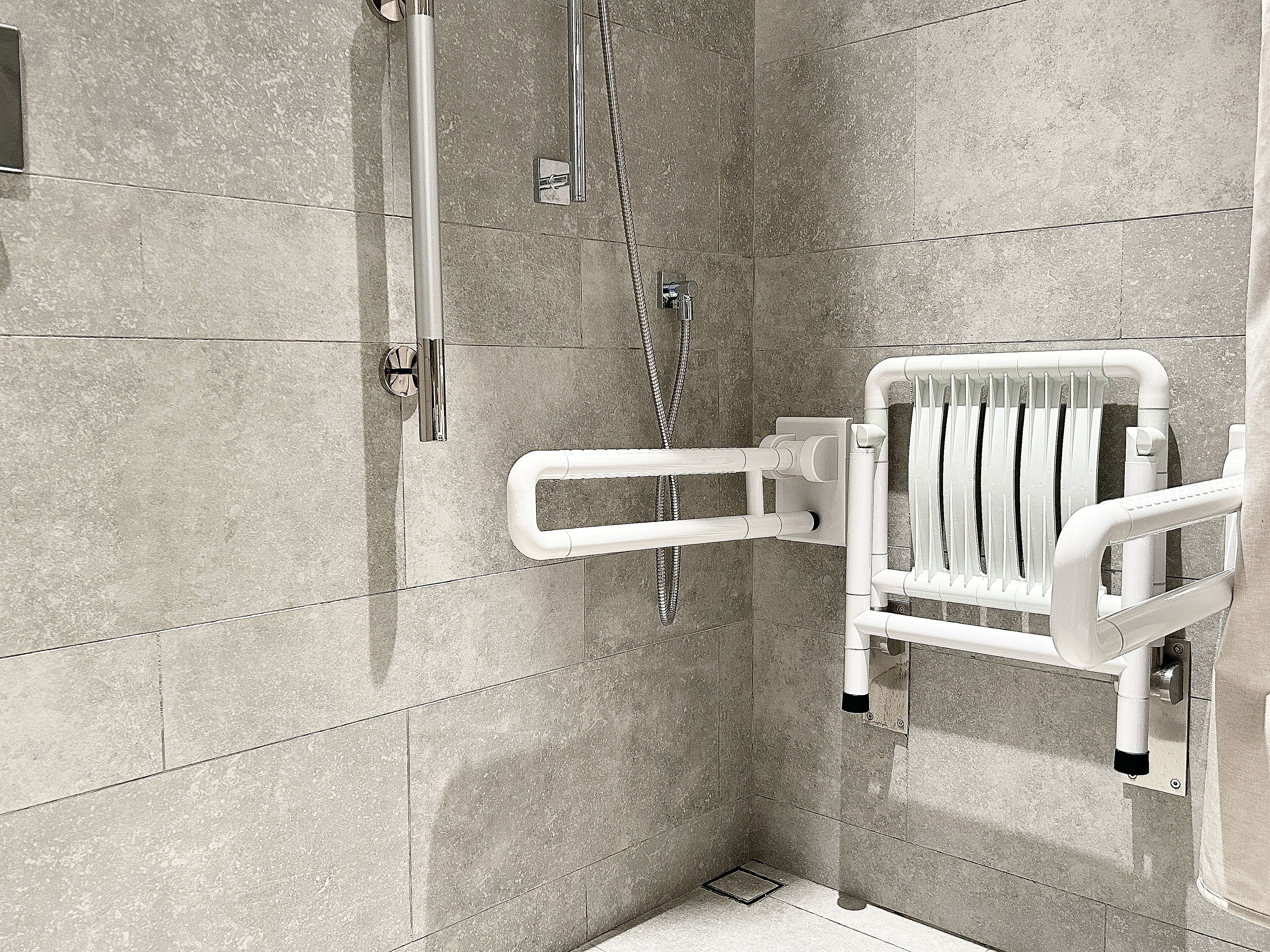 A shower area with a white grab bar and a handheld showerhead.