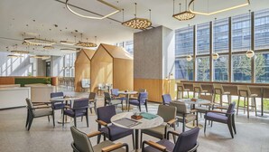 Un espace intérieur moderne doté de nombreuses tables et chaises, de grandes fenêtres et d’un éclairage contemporain.