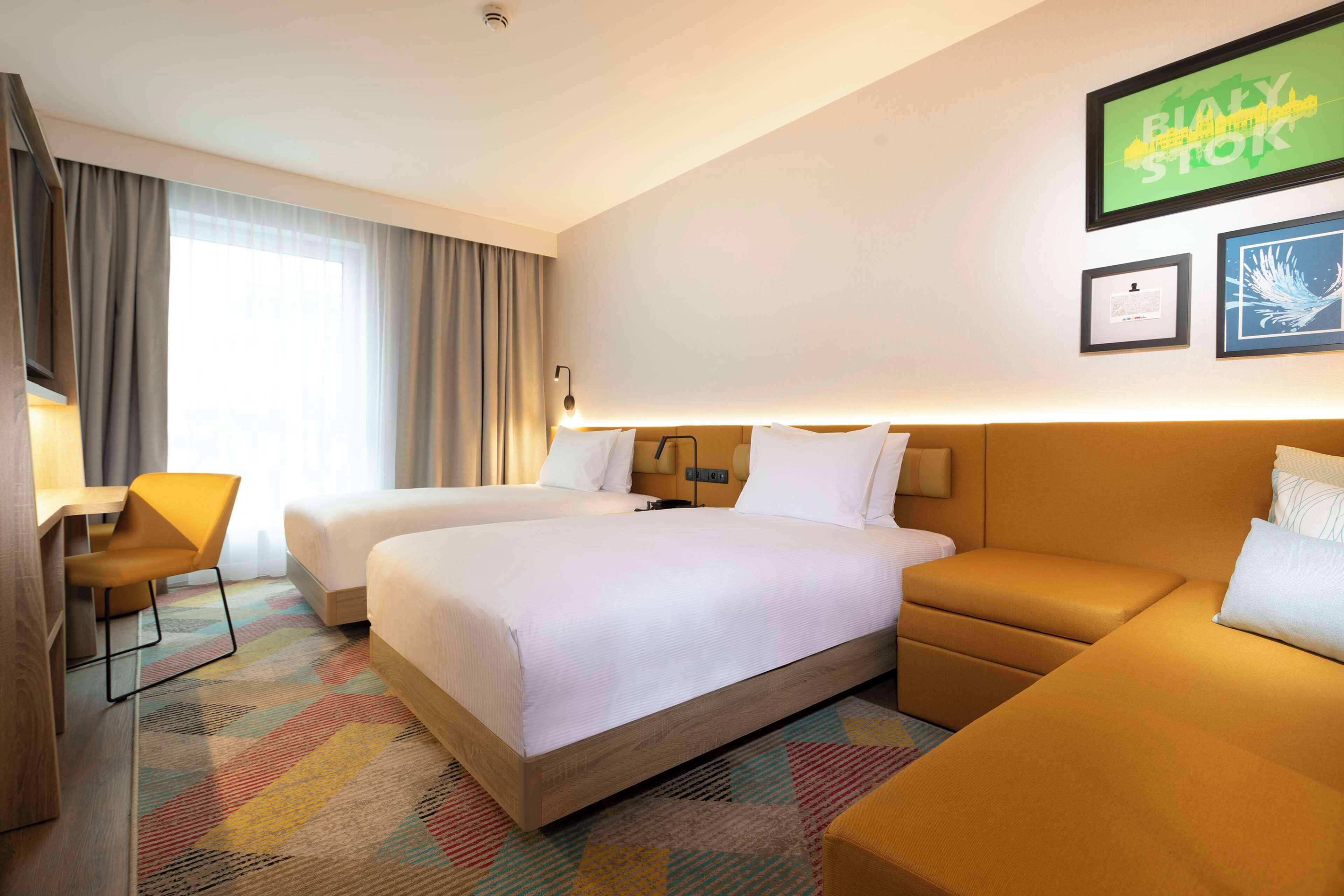 A hotel room with two beds, a desk, and a sofa.