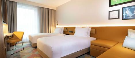 A hotel room with two beds, a desk, and a sofa.