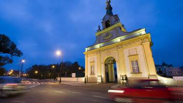 A historic building with a prominent clock tower and arched entrance, surrounded by a well-lit street at dusk.