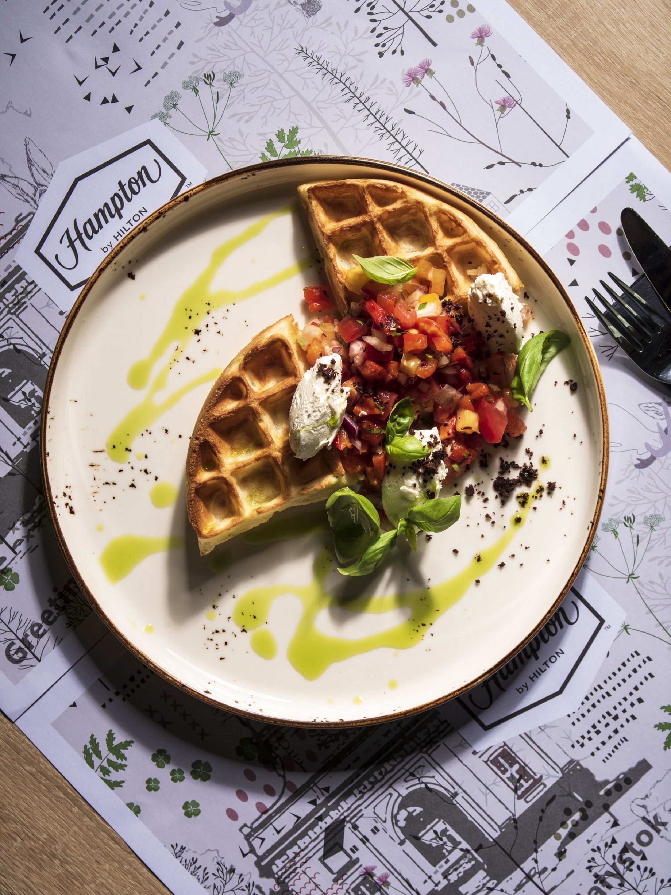 Een bord met een wafel, een tomatensaus en een toefje slagroom, geserveerd op een wit bord met een groene garnering.