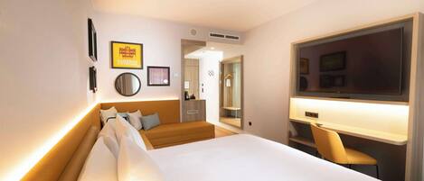 Quarto de hotel com uma cama grande, uma escrivaninha com cadeira, uma televisão e um espelho.