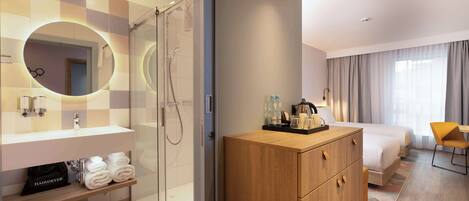 A modern hotel room with a shower, a large mirror, a wooden wardrobe, a bed, and a small seating area.
