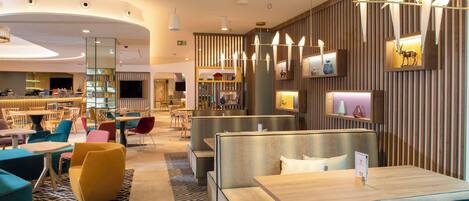 A modern hotel lobby with seating areas, a bar, and a reception desk.