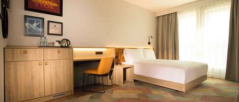 A hotel room with a bed, desk, chair, and a large window with curtains.