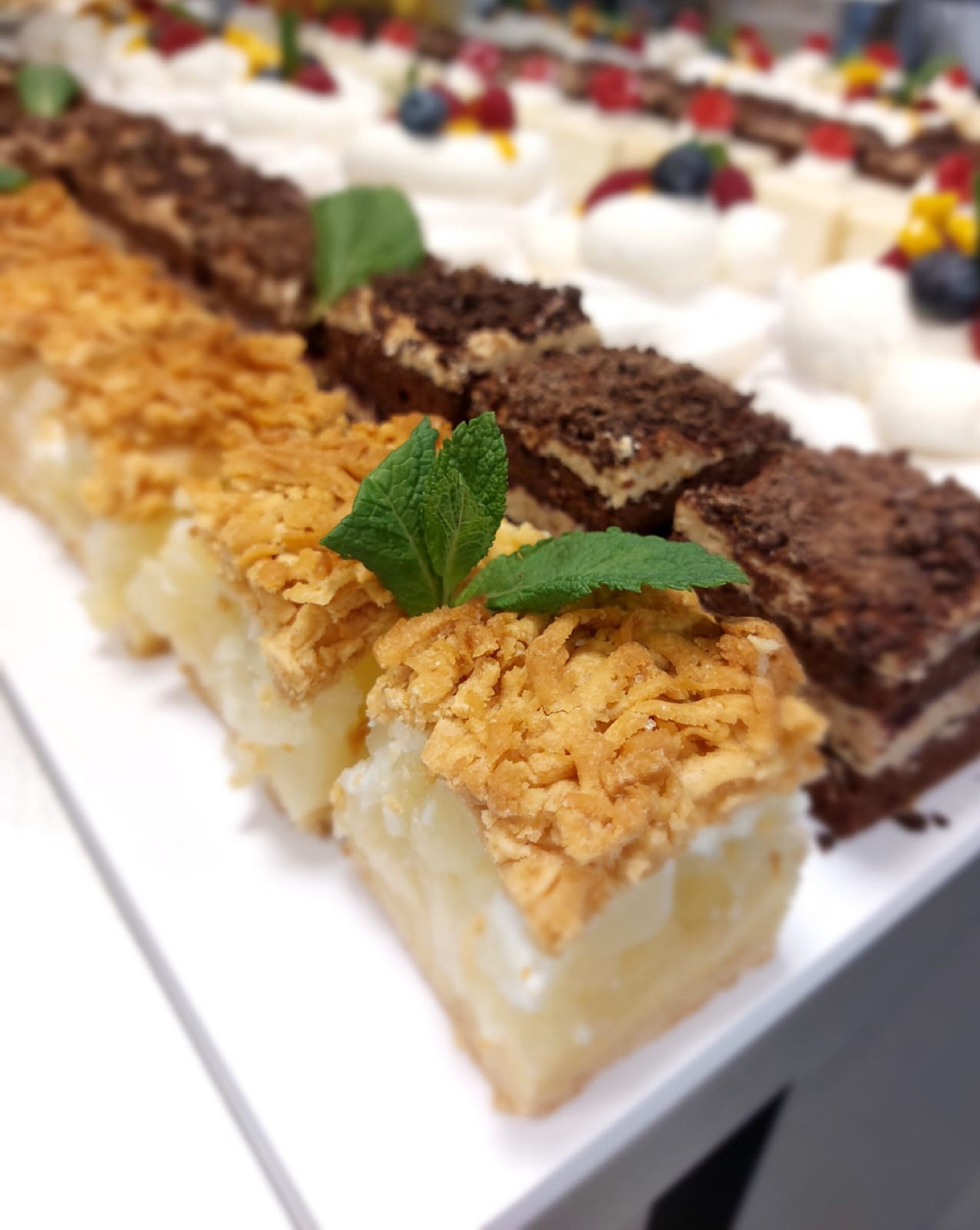 A dessert tray with various cakes and pastries, including a cake with a golden crumble topping and a mint leaf garnish.