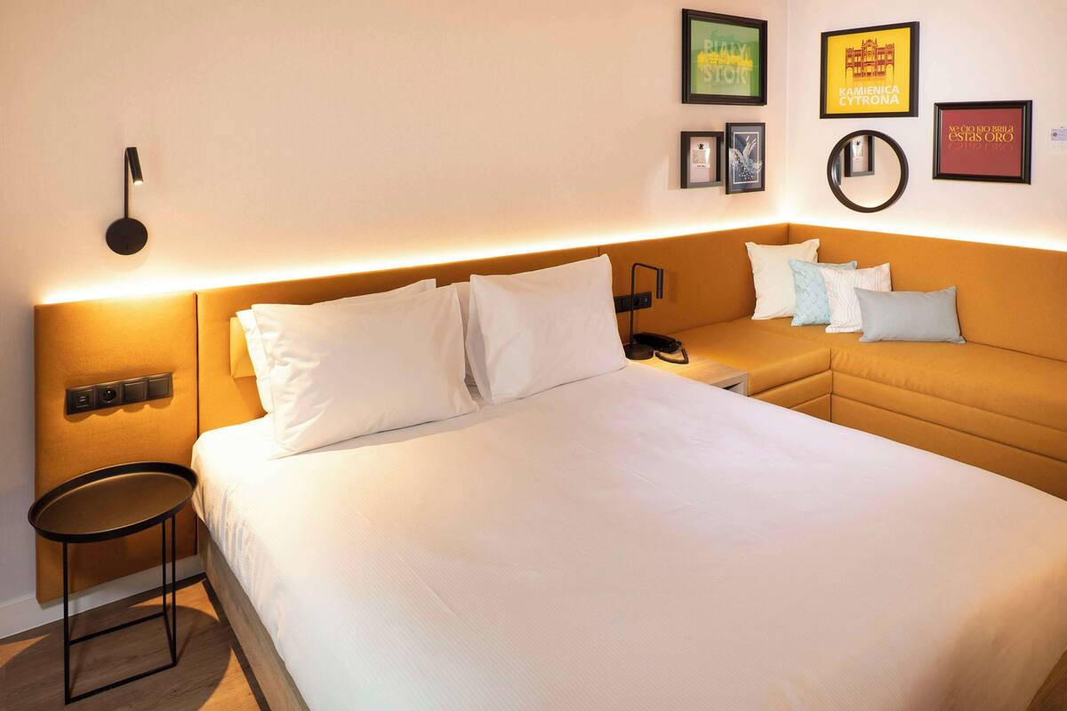 Une chambre d’hôtel avec un grand lit, un petit canapé, une table de chevet et une lampe fixée au mur.