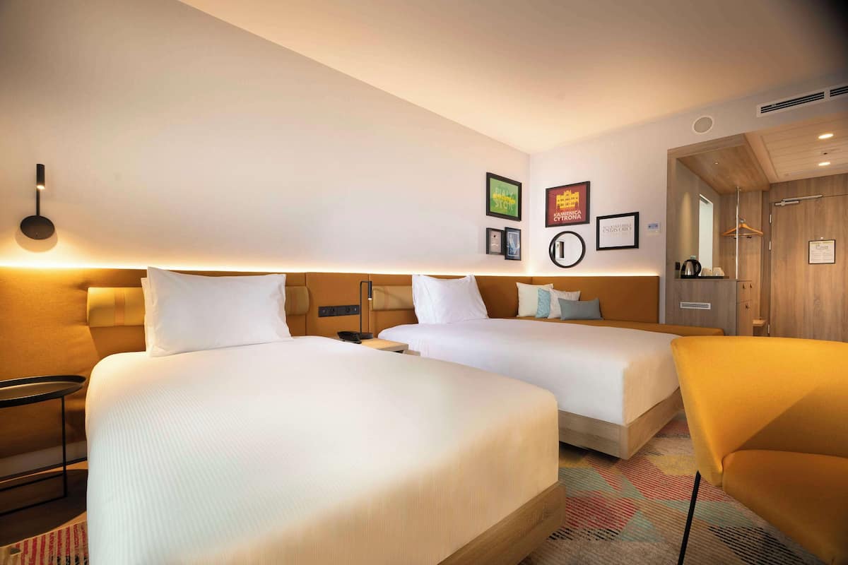 Une chambre d’hôtel avec deux lits, un canapé, une petite table et un téléviseur fixé au mur.