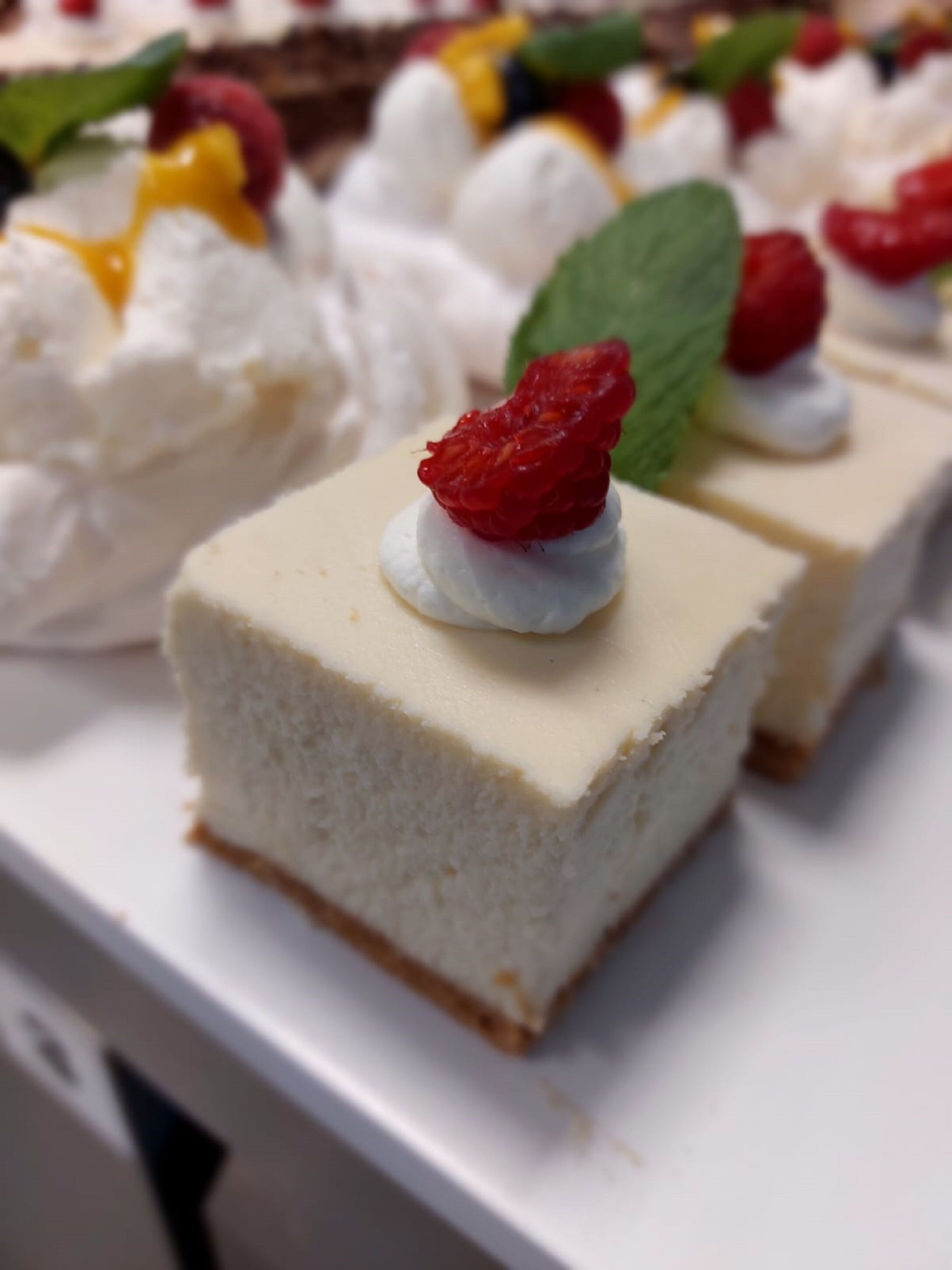 Uma bandeja de sobremesas com fatias de cheesecake cobertas de chantilly e uma morango, além de um toque de hortelã.