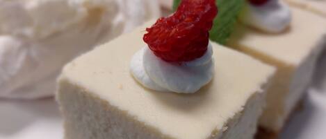 Uma bandeja de sobremesas com fatias de cheesecake cobertas de chantilly e uma morango, além de um toque de hortelã.