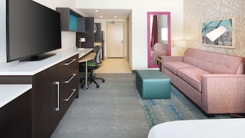 A hotel room with a large flat-screen TV, a desk with a chair, a sofa, a small table, and a mirror.