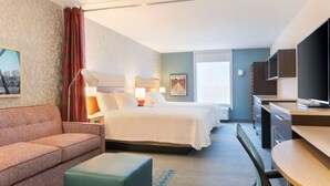 A hotel room with a bed, a sofa, a desk, and a TV.