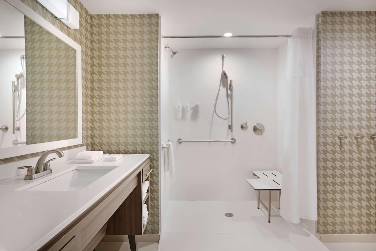 Un bany modern amb un mirall gran, un lavabo, una dutxa amb plat de roba i un petit tocador.