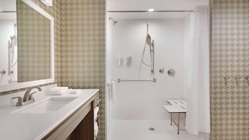 Uma casa de banho moderna com um espelho grande, uma pia, chuveiro com chuveiro manual e uma pequena mesa de toucador.