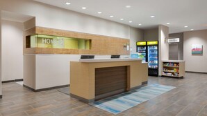 A hotel reception area with a reception desk, a minibar, and a self-service beverage station.